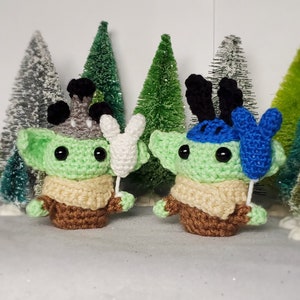 May include: Two green crocheted plush toys with large eyes and brown yarn clothing. One toy is holding a white crocheted balloon and the other is holding a blue crocheted balloon.