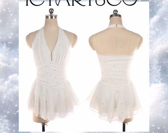 May include: A white figure skating dress with a halter neckline and a flowing skirt. The dress is adorned with small, sparkling embellishments. The text "ICYARTSCO" is displayed at the top of the image.