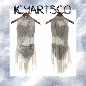 May include: Two gray dance leotards on wooden hangers. One features a high neck, sheer panels, and white floral embellishments. The other has a keyhole back and a sheer skirt. The text "ICYARTSCO" is at the top.