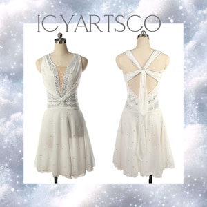 Könnte beinhalten: Weißes ärmelloses Kleid mit V-Ausschnitt und fließendem Rock. Das Kleid ist mit silbernen Verzierungen am Ausschnitt und am Oberteil versehen. Der Rücken des Kleides hat ein Schlüsselloch-Design mit einer Schleife. Der Text "ICYARTSCO" steht oben.