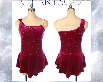 Puede incluir: Un vestido de patinaje artístico de terciopelo burdeos con un diseño de un solo hombro y una falda corta. El vestido está decorado con pequeños diamantes de imitación blancos.