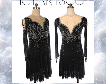 May include: A black figure skating dress with long sleeves and a V-neckline. The dress is embellished with rhinestones and has a sheer overlay. The dress is on a mannequin.