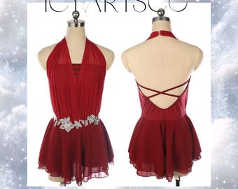 Puede incluir: Un vestido de baile de color burdeos con tirantes, con un adorno floral plateado en la cintura. El vestido tiene un diseño de espalda cruzada y una falda fluida.