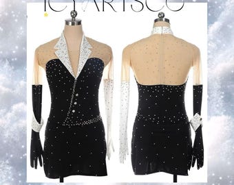 May include: Black figure skating dress with a white collar and long sleeves. The dress is decorated with rhinestones and has a sheer overlay. The dress is shown on a mannequin.