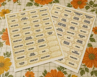 Puede incluir: Dos hojas rectangulares de etiquetas adhesivas para especias con un fondo crema de estilo vintage y bordes dorados ornamentados. Cada etiqueta contiene texto impreso en negro que identifica varias especias y hierbas como Allspice, Basil, Cloves y Cinnamon.