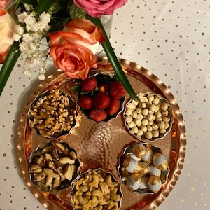 Może przedstawiać: Miedziana taca serwująca z sześcioma małymi miseczkami wypełnionymi różnymi przekąskami, w tym truskawkami, orzechami włoskimi, laskowymi, nerkowcami, orzechami brazylijskimi i cukierkami w czekoladzie.