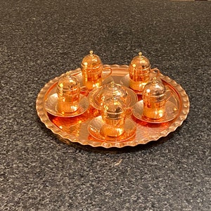 May include: A set of six copper Turkish coffee cups and saucers on a decorative copper tray. The cups have a hammered finish and are adorned with gold accents.