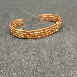 May include: A copper bracelet with a braided design and gold accents.