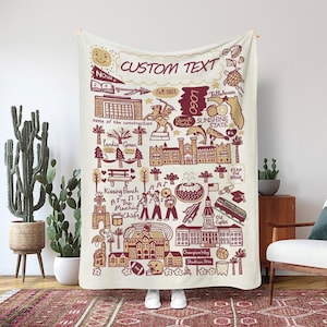 May include: Cream-colored throw blanket with a maroon and tan illustrated design. The design includes the text "CUSTOM TEXT", "NOLES", and "SUNSHINE STATE", along with various drawings of buildings, landmarks, and symbols.