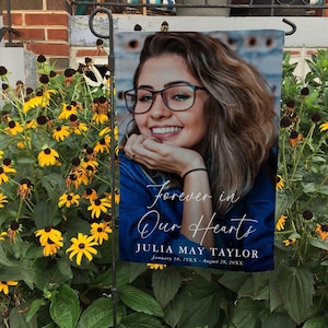 May include: A memorial garden flag with a photo of a woman wearing glasses and a blue shirt. The text reads "Forever in Our Hearts Julia May Taylor January 18, 19XX - August 28, 20XX".