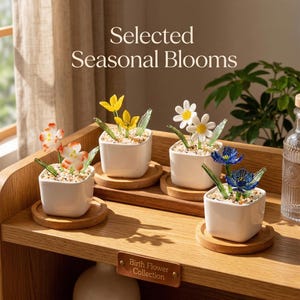 May include: Four small, square white ceramic pots with colorful glass flower arrangements sit on wooden coasters. The flowers include orange, yellow, white, and blue blooms. The text "Selected Seasonal Blooms" is at the top.