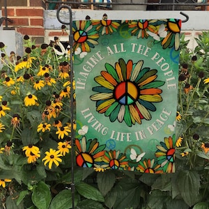 May include: A green garden flag with a peace sign and the text "Imagine all the people living life in peace". The peace sign is surrounded by colorful flowers and butterflies.