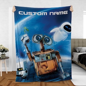May include: A blue blanket featuring the characters Wall-E and Eve from the animated movie. The blanket has the text "CUSTOM NAME" at the top. Wall-E is holding a plant, and Eve is floating in the background. The blanket is displayed on a bed.