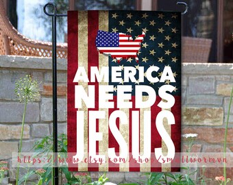 May include: A red, white, and blue American flag with a distressed look. The flag has a white outline of the United States with stars on a blue background. The text "America Needs Jesus" is printed in white on the flag.