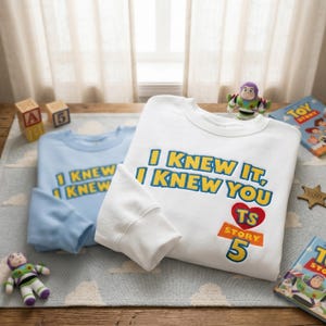 Puede incluir: Una sudadera blanca de cuello redondo con el texto I KNEW IT, I KNEW YOU, un coraz&oacute;n rojo con las letras TS y el texto STORY 5 en azul, amarillo y naranja. Una sudadera azul claro con el mismo texto se encuentra detr&aacute;s de la blanca.
