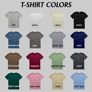 May include: A grid of t-shirts in various colors, including ash, white, beige, and black. Other colors are Carolina blue, grey, sport grey, navy, chocolate, maroon, military green, wash, forest green, light pink, sand, and light blue. Text at the top reads "T-SHIRT COLORS."