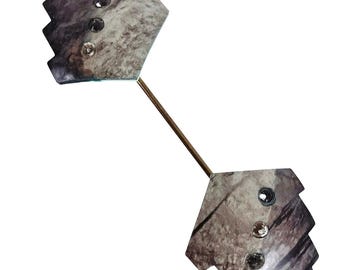 May include: A barbell-shaped lapel pin with a marbled grey and brown design. Each end features three clear, round embellishments. The pin is connected by a thin, gold-coloured bar.