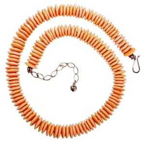 Peut inclure: Un collier composé de perles en forme de disques de couleur pêche, enfilées ensemble. Le collier est doté d'une chaîne et d'un fermoir argentés. Les perles sont de taille et de forme uniformes, créant un design lisse et incurvé.