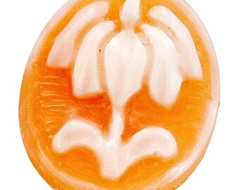 May include: An oval-shaped, orange-colored object with a white floral design in the center. The design features a central, elongated shape with petal-like elements extending outwards. The object has a smooth, glossy appearance.