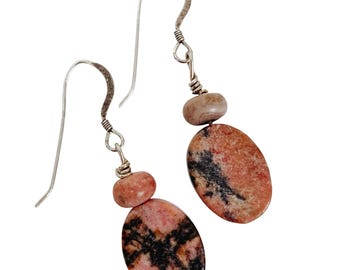 May include: Dangle earrings with oval pink and black stones, complemented by smaller pink and tan beads. The earrings have silver-coloured ear wires and connecting elements. A natural stone jewellery design.