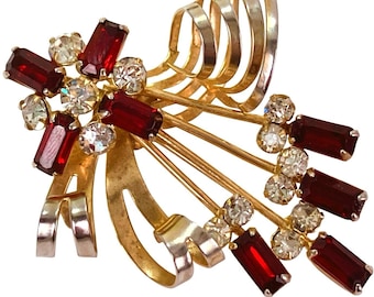 Pode incluir: Broche vintage dourado com design floral. O broche apresenta strass retangulares vermelhos e redondos transparentes. O design inclui elementos de metal dourado curvos e um fecho de alfinete na parte de trás.