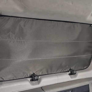 May include: A grey mesh window blind is fitted in a vehicle. The blind is secured by two black clips on each side. The blind is designed to block out sunlight and provide privacy.