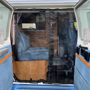 May include: A blue van with the doors open, revealing the interior. The interior has a wooden floor and a blue seat. There is a black mesh screen covering the doorway.