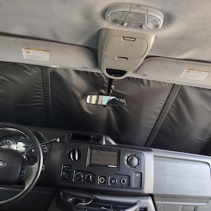 May include: The interior of a van with black window shades, a steering wheel, and a dashboard with controls. The dashboard has a radio, climate controls, and a blank screen.