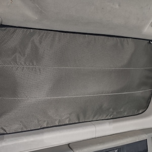 May include: A grey window blind with a black border and a white mesh pattern. The blind is fitted in a vehicle.