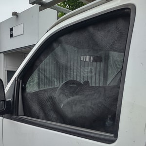 Puede incluir: Una furgoneta blanca con una pantalla de ventana de malla negra instalada. La pantalla está bajada y cubre toda la ventana. La furgoneta está estacionada frente a un edificio con el número "324" en la pared.