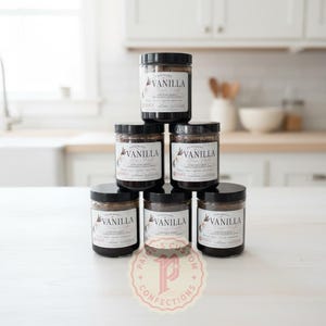 May include: A pyramid stack of six clear glass jars filled with dark brown vanilla bean paste. Each jar features a white label with black text reading Homemade Vanilla Bean Paste and Paige's Custom Confections, with a logo of a stylized letter P.