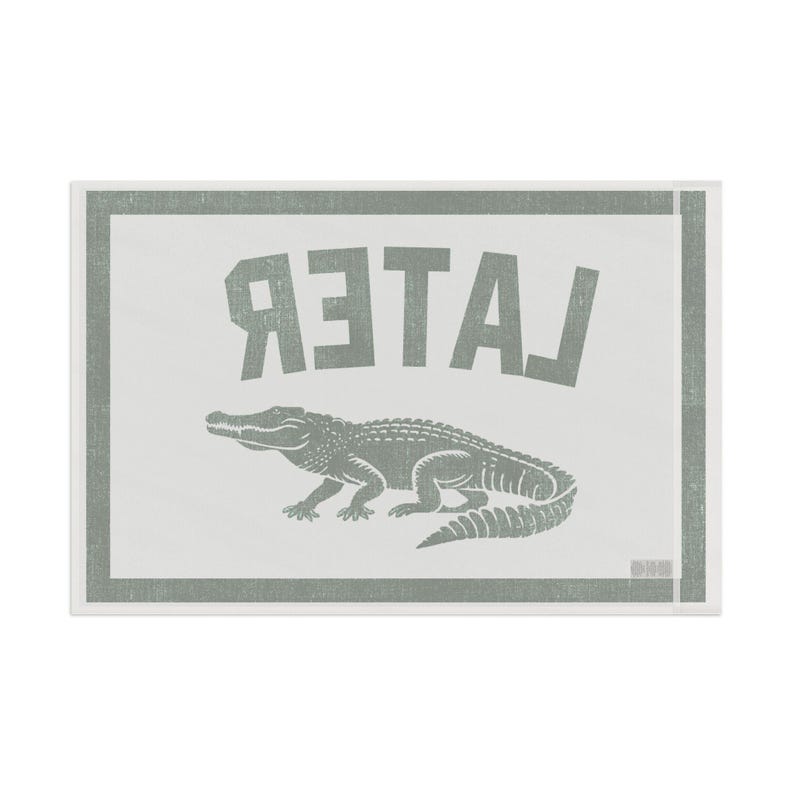 May include: A rectangular, off-white sign with a gray border and text. The word "LATER" is printed in large, gray, reversed letters above a gray alligator illustration. The design has a vintage, screen-printed aesthetic.