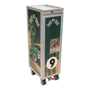 May include: A silver rolling cart with a green, brown, and white graphic design featuring a vintage car, a woman wearing sunglasses, and checkered flags. The cart has a number "9" on the front and a handle on the side.