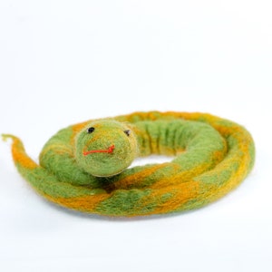 May include: A green and orange felt snake toy curled up in a circle. The snake has a small, round head with black eyes and a red mouth.