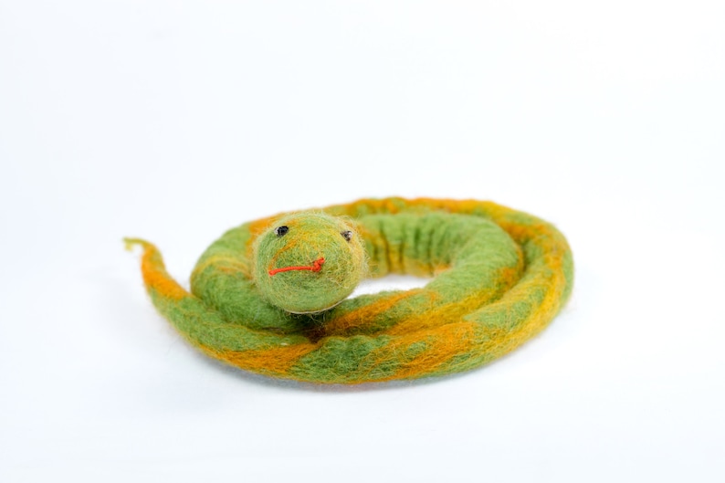 May include: A green and orange felt snake toy curled up in a circle. The snake has a small, round head with black eyes and a red mouth.