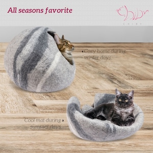 May include: A gray and white felt cat bed with a cat curled up inside. The bed is shaped like a bowl and has a raised edge. The text "Cozy home during winter days." is written on the right side of the image. The text "Cool mat during summer days." is written on the left side of the image.