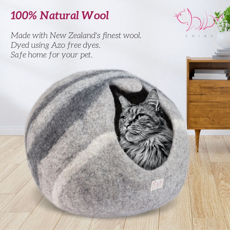 May include: A gray and white wool cat bed shaped like a sphere with a cat peeking out of the opening. The bed is made with 100% natural wool from New Zealand and is dyed with azo-free dyes. The text "100% Natural Wool" is at the top of the image. The text "Made with New Zealand's finest wool. Dyed using Azo free dyes. Safe home for your pet." is below the image of the cat bed.