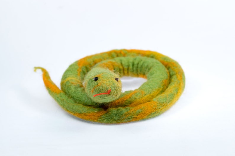 May include: A green and yellow felt snake toy with a curled body and a black eye. The snake has a red mouth.