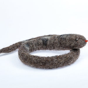 May include: A grey felt snake toy with a red tongue. The snake is curled into a circle.