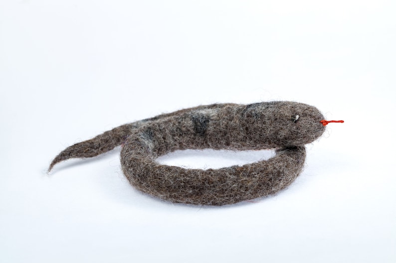 May include: A grey felt snake toy with a red tongue. The snake is curled into a circle.