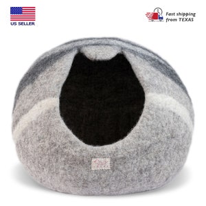 May include: A gray and white felt cat bed shaped like a dome with a black felt interior. The bed has a small pink label with the word "Chiev" on it.