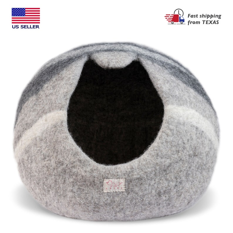 May include: A gray and white felt cat bed shaped like a dome with a black felt interior. The bed has a small pink label with the word "Chiev" on it.