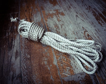 May include: A coiled length of thick, light beige natural fibre rope. The rope features a twisted construction with a visible texture and a knotted end, arranged in a series of overlapping loops that form a compact, elongated bundle.
