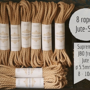 Könnte beinhalten: Ein Set aus acht aufgewickelten beigen Juteseilen, die jeweils mit einer weißen Papierbanderole mit dem Text VÆGABØUND versehen sind. Das Bild enthält Text mit der Angabe 8 ropes Jute-Set, Supreme JBO free Jute, 5,5 mm Durchmesser und 8-10 m.