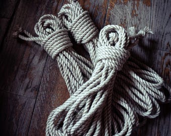 May include: Two bundles of thick, natural-coloured twisted fibre rope. Each bundle is coiled and secured with a tight wrap of the same rope material, featuring frayed ends at the top of each coil. The texture is rough and fibrous.