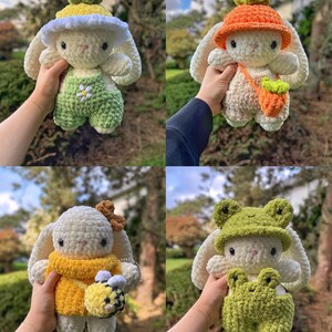 May include: Four crocheted bunny plushies with different outfits. The first bunny is wearing a green and white outfit with a yellow flower hat. The second bunny is wearing an orange hat and a brown bag. The third bunny is wearing a yellow sweater and holding a bee. The fourth bunny is wearing a green frog hat and a green frog outfit.