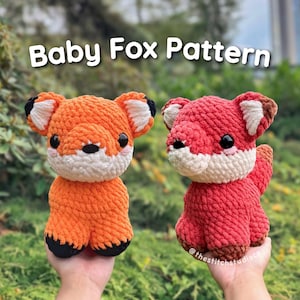 May include: Two crocheted baby fox plushies, one orange and one red, with black eyes and white noses. The text "Baby Fox Pattern" is displayed above the plushies.