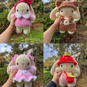 May include: Four crocheted bunny plushies in different outfits. The first bunny is wearing a pink dress and a red bow. The second bunny is wearing a brown jumpsuit and a brown bear hat. The third bunny is wearing a pink dress with white trim. The fourth bunny is wearing a red strawberry hat and a pink dress with a strawberry purse.