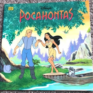 Può includere: Un'edizione vintage di Disney's Pocahontas di Golden Books. La copertina presenta un'illustrazione colorata di Pocahontas e John Smith che si tengono per mano, con un procione in una canoa. Il titolo è in grandi lettere vivaci.