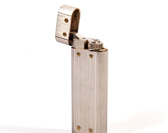 May include: A silver-colored lighter with a rectangular body and a hinged top. The lighter is open, revealing the internal mechanism. The surface has vertical brushed lines, and small screws secure the components. The lighter is set against a white background.